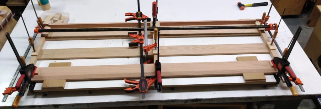 A wooden pew back secured with clamps on a workbench inside a clamping fixture after the glue-up process.