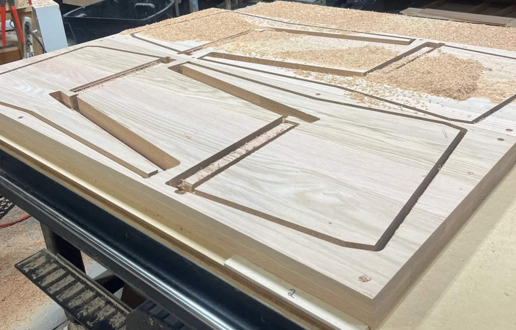 Large oak slabs clamped to a CNC router bed after being milled into the shapes of the pew ends.
