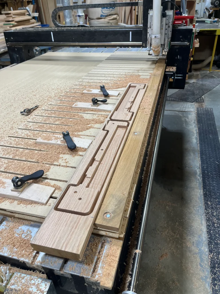 Several wooden pew feet halves milled from a narrow oak board, still held by tabs on a CNC router bed.