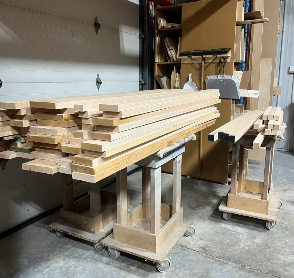 Three carts loaded with rough-cut oak lumber in a woodworking shop, ready for processing.