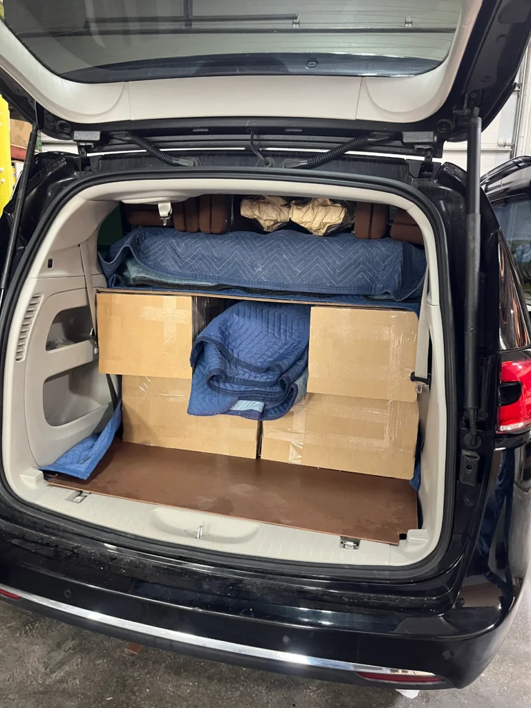 Custom pews for the Holy Cross Chapel flat-packed and protected with moving blankets and cardboard, tightly loaded into a Chrysler Pacifica for transport.